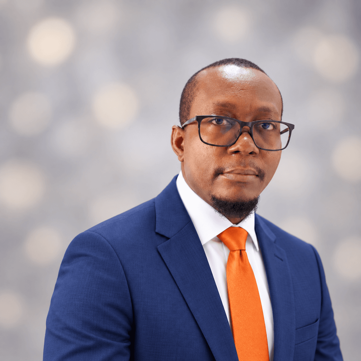Homme professionnel en costume bleu et cravate orange portant des lunettes sur fond flou.